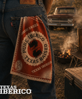 Person holding a 'Pure Iberico Texas Raised' towel with a rustic outdoor setting featuring a truck and campfire.