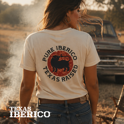 Person wearing a 'Pure Iberico Texas Raised' t-shirt in a rural setting with a truck in the background.