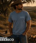 Man wearing a blue 'Texas Iberico' t-shirt in a natural setting with 'Texas Iberico' branding.