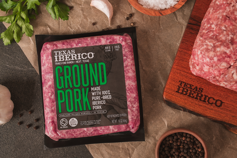 Packaged ground pork from Texas Iberico on a wooden surface with ingredients.