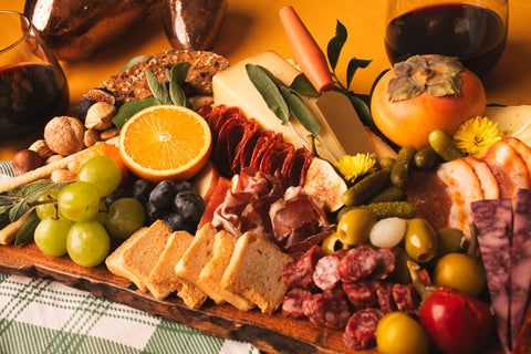 Wooden charcuterie board with meats, cheeses, fruits, and bread on a checkered tablecloth.